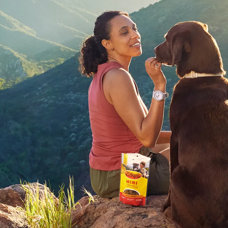 Woman feeding dog Zuke's treats on a hike